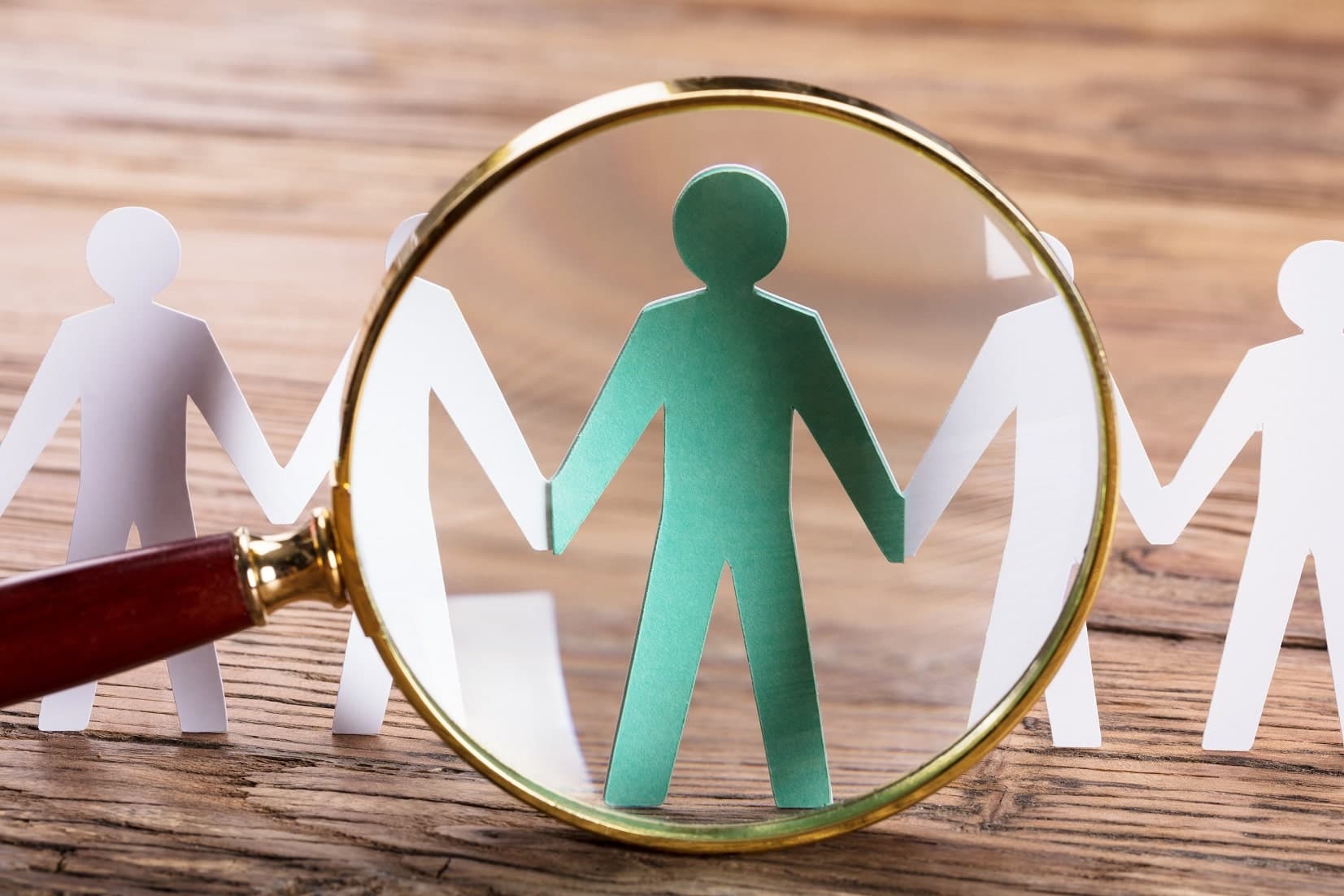 A magnifying glass highlighting one figure among a row of paper figures holding hands