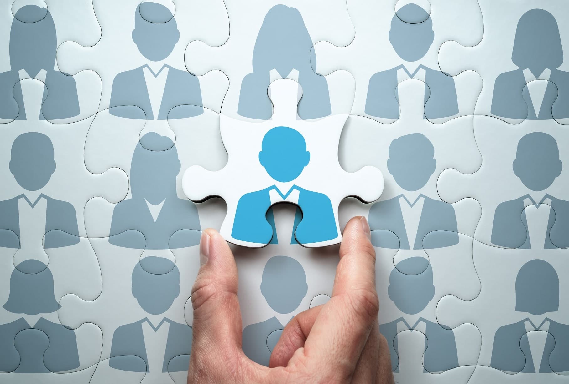 A hand placing a jigsaw puzzle piece showing a person icon among a crowd of silhouettes